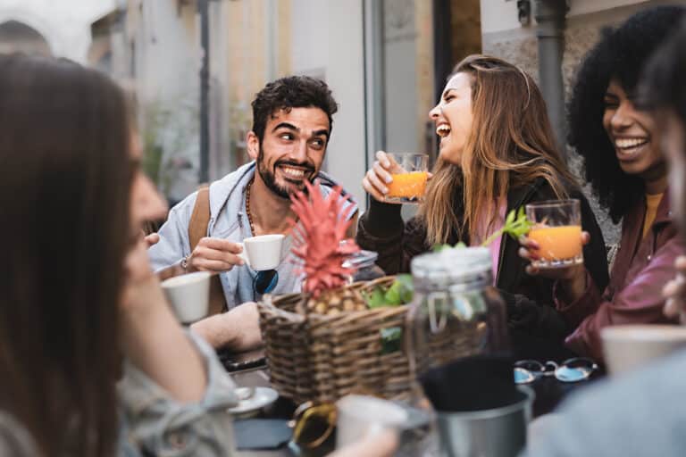 Black and white cheerful mates laughing enjoying meal having fun sitting together at restaurant table - Food and beverage lifestyle concept on young people enjoying time together outside